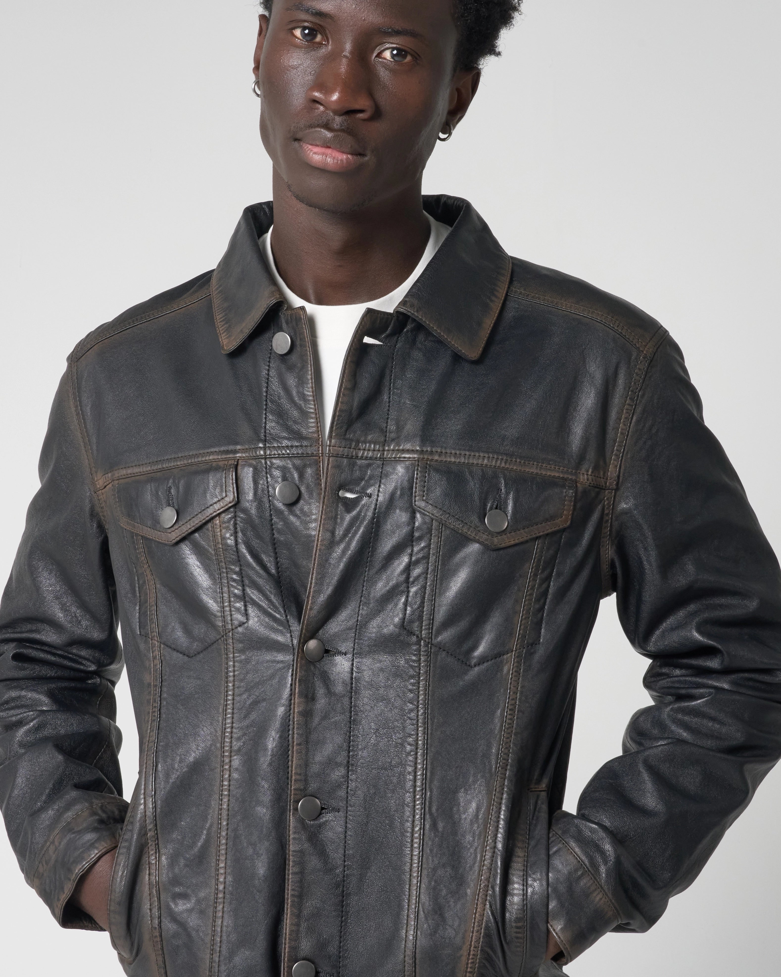 Cropped image focusing on leather trucker jacket as worn by male model. He puts his hands in his pockets and the jacket is halfway buttoned up.