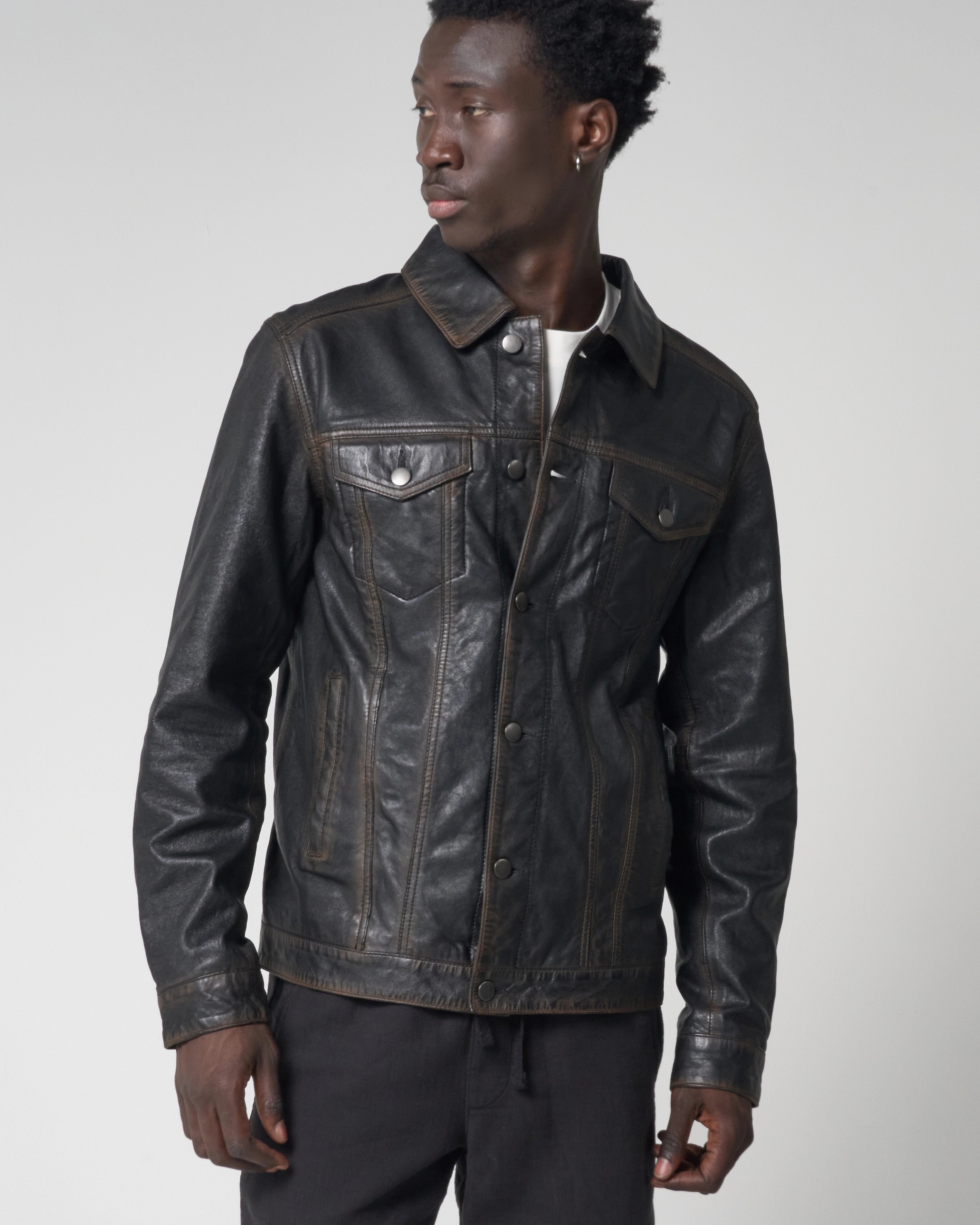 A man wearing a black distressed leather jacket with a collar, button front, and chest flap pockets. The jacket is buttoned up to show the jacket closed.