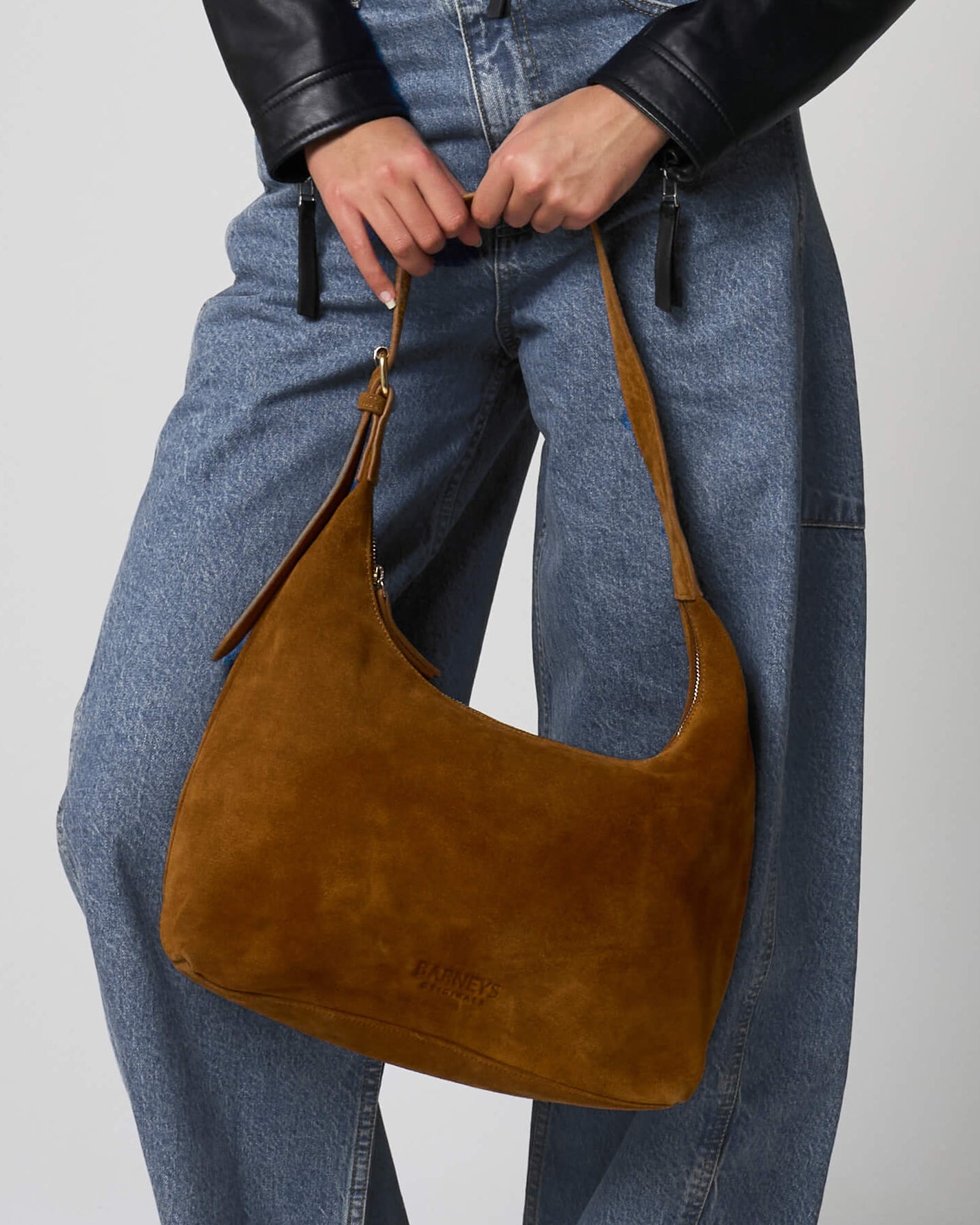 Tan suede bag held by a woman wearing blue jeans.