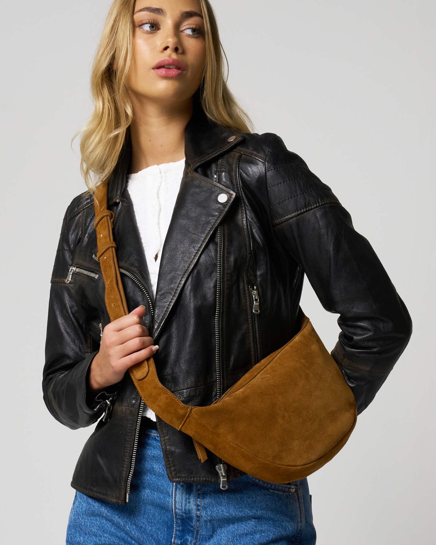 Woman wears a tan suede bag, the strap is worn across the body.