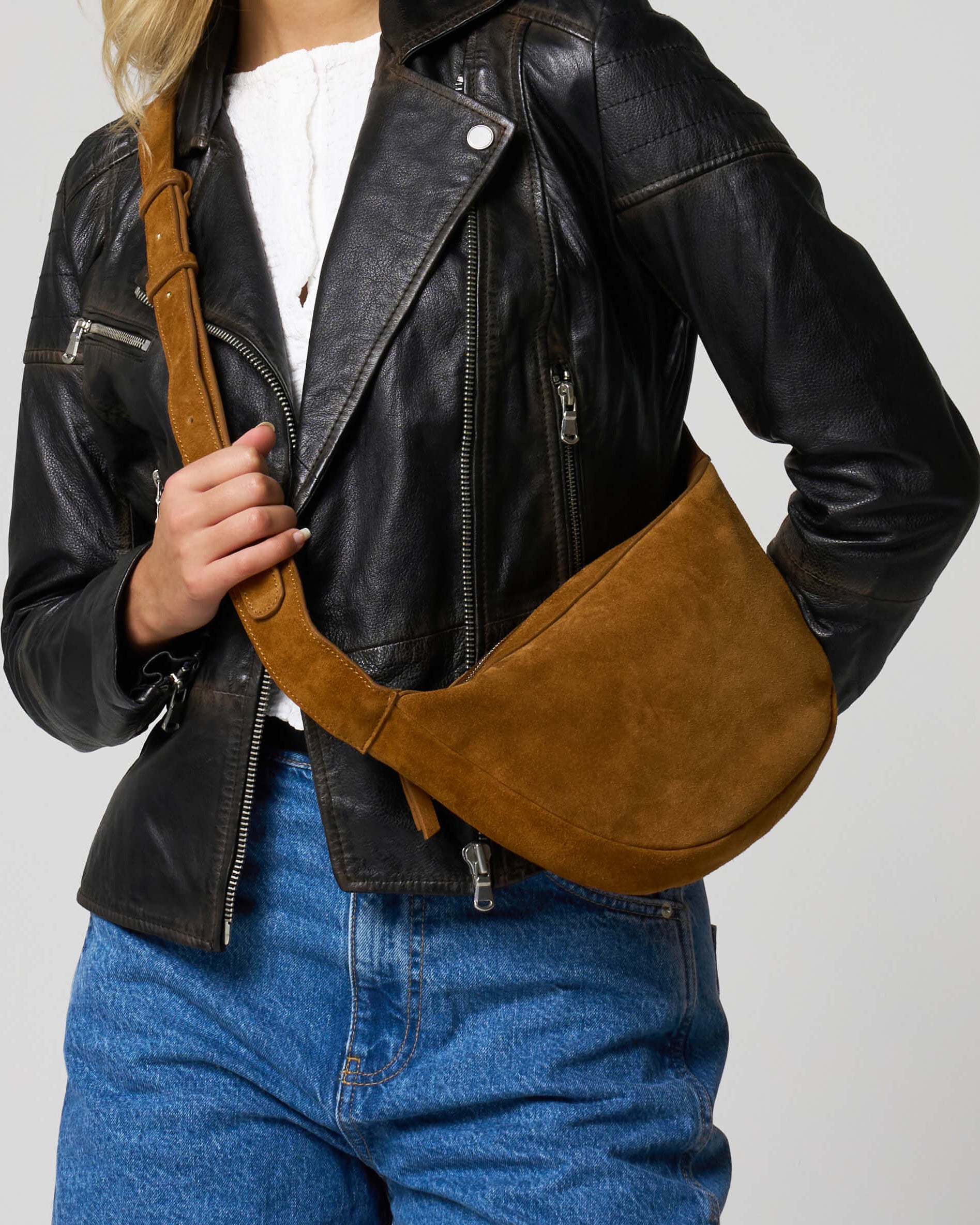 Mid body shot of a model wearing the tan suede cross body bag from Barneys Originals.