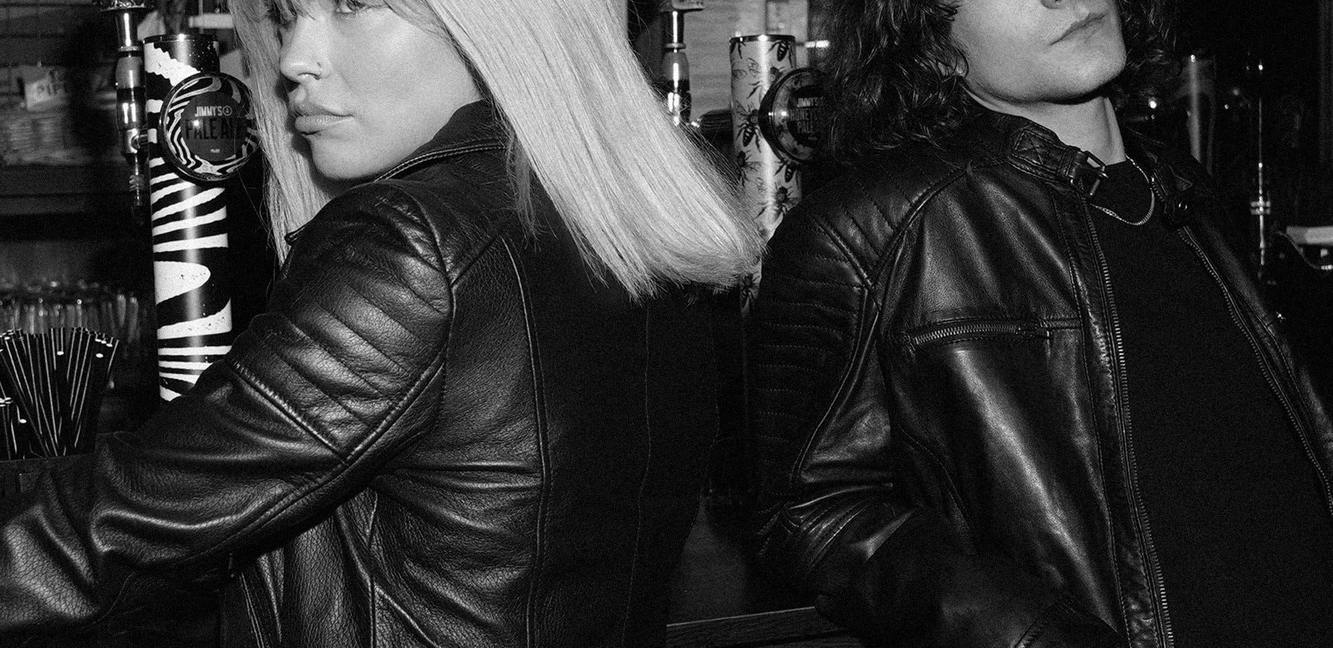 Image displays a woman and a man waiting to be served at a bar - they both wear leather jackets.