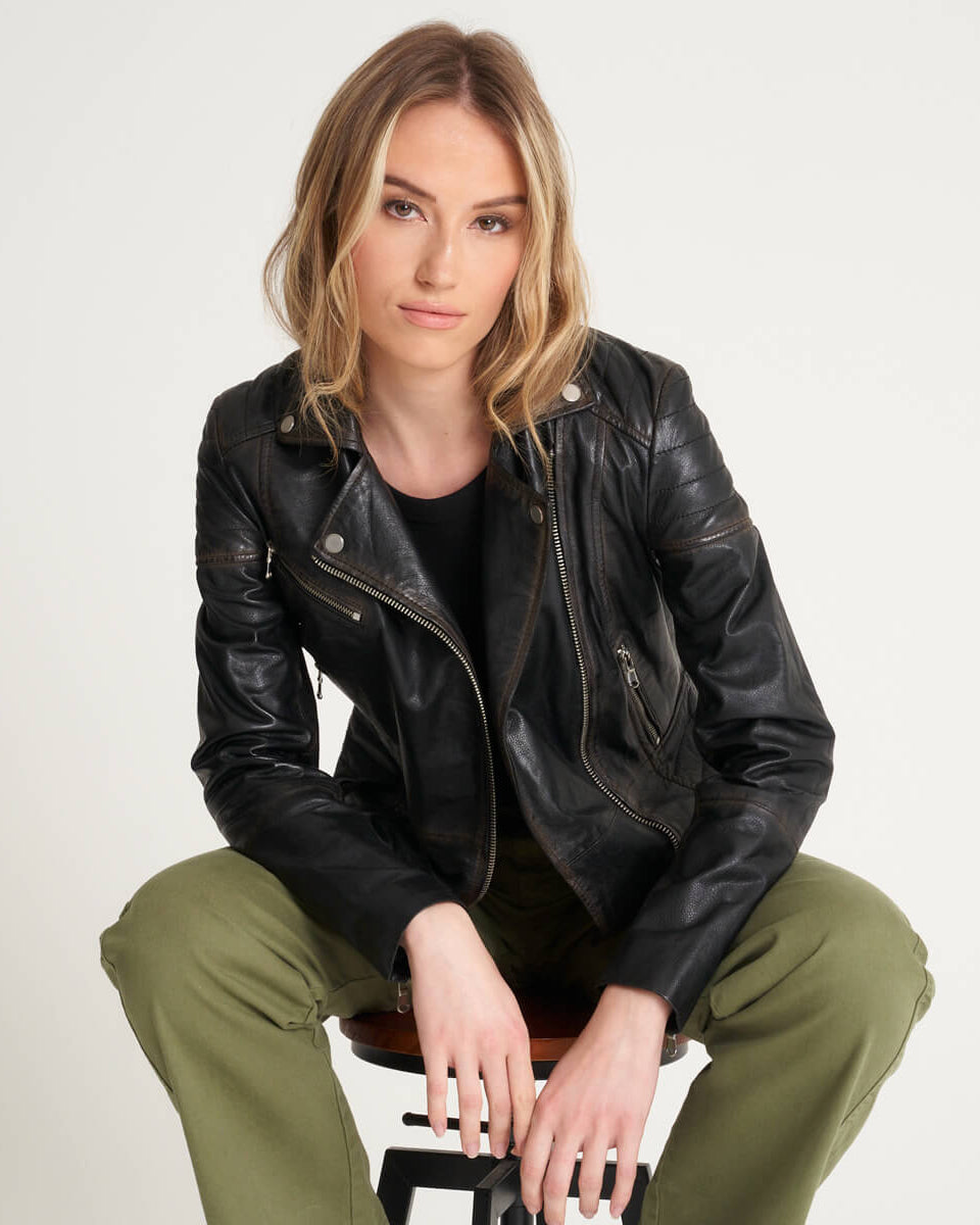 Woman sitting on a chair wearing a leather biker jacket with washed vintage detailing.